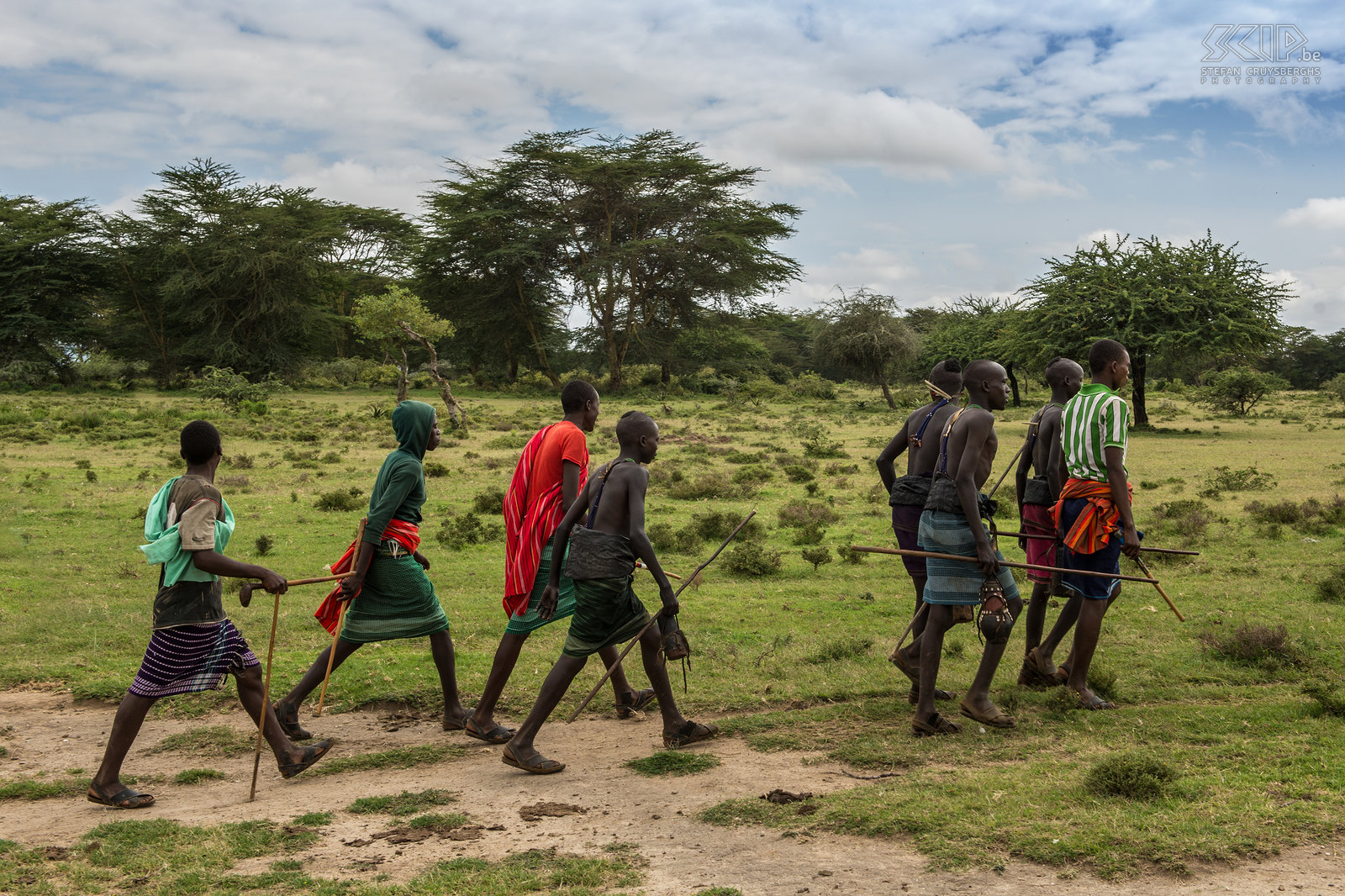 Kisima - Toekomstige morans Om de 6 à 10 jaar organiseren de Samburu clans een lmuget-ceremonie voor de overgang naar een volgende leeftijdsgroep. Jonge mannen van 14 tot 20 jaar worden besneden en worden daarna moran (krijger). Dit is de belangrijkste gebeurtenis in het leven van een jonge Samburu. <br />
<br />
De dagen voor de lmuget ceremonies verlaten ze de lorora (het tijdelijke dorp) en in groep gaan ze al zingend op pad om water en kruiden te verzamelen. Sommigen van hen dragen nog steeds de traditionele door-houtskool-zwartgeblakerde-mantel rond hun middel. Ze zingen de lebarta, een speciaal lied voor de besnijdenis. Stefan Cruysberghs